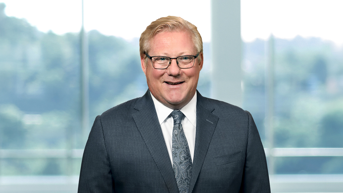 Executive Leadership Team: Portrait of Scott A. Smith, Chief Executive Officer, a middle-aged man with glasses wearing a grey suit, standing in front of a blurred office background.